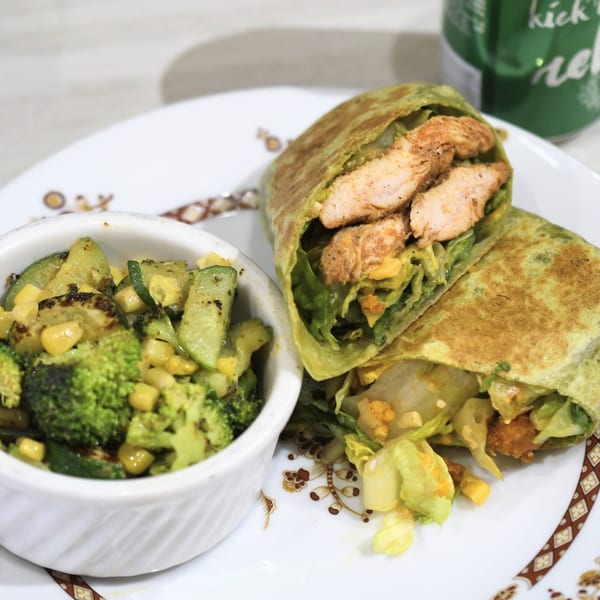 A chicken wrap with lettuce and corn, served with a side of roasted broccoli, zucchini, and corn.