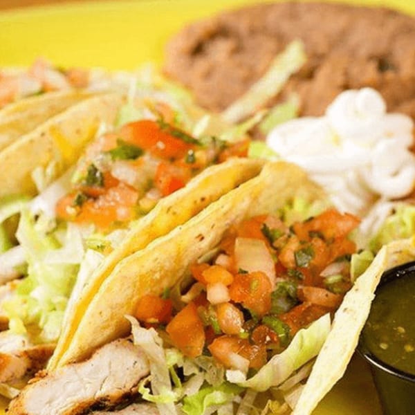 Three chicken tacos with lettuce, pico de gallo, sour cream, and a side of salsa verde.