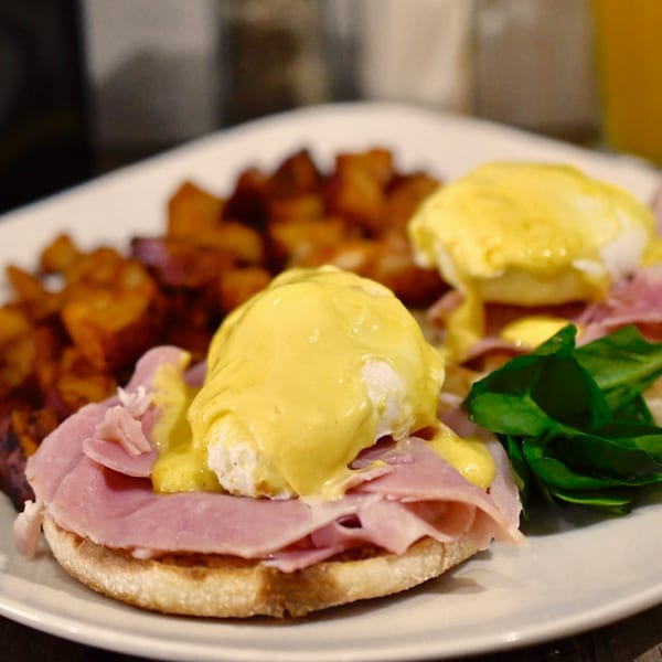 Janik's Cafe Eggs Benedict with ham, hollandaise, and a side of roasted potatoes and spinach.